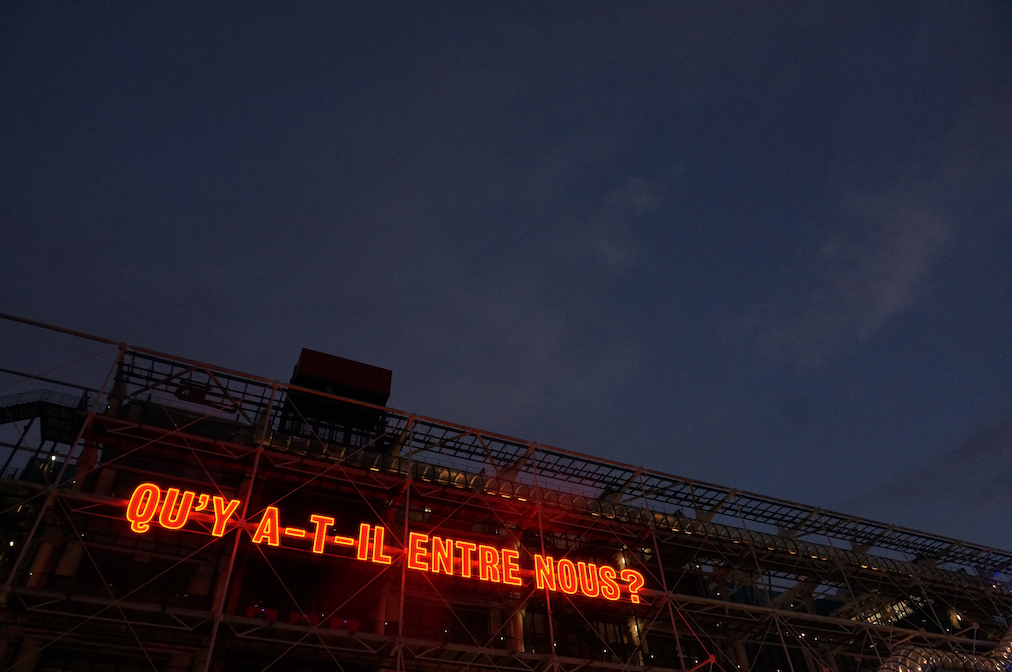 In red neon letters reads 'OU'Y A-T-IL ENTRE NOUS?' on the side of the Centre Pompidou in Paris.