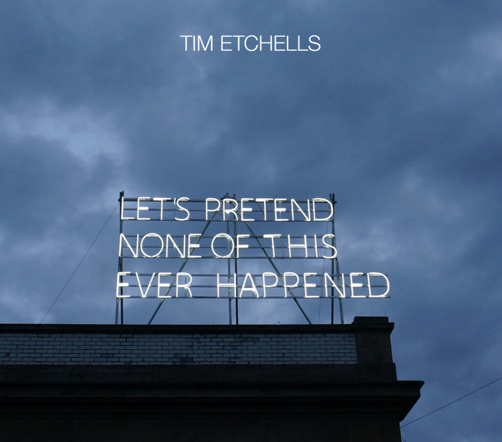 White neon letters on top of a building infront of a cloudy sky reads 'Lets pretend none of this ever happened'.